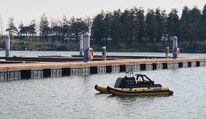 A yellow and black underwater inspection boat named charpie moored on a dock, surrounded by calm water and a sunny atmosphere.